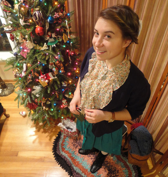 Julia sports a floral top, a navy cardigan, her green pocketed skirt, white tights, and black boots.